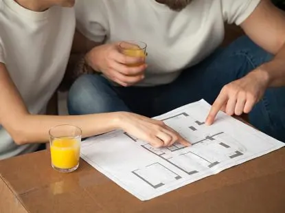 זוג בחולצות לבנות שותה מיץ תפוזים ומסתכל בתרשים דירה