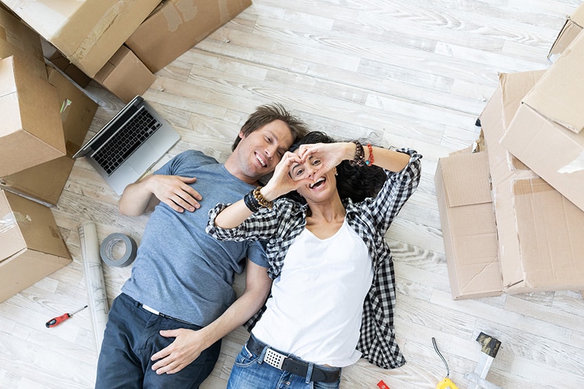 זוג צעיר מאושר שוכב על רצפת פרקט ומסביבו ארגזי מעבר דירה